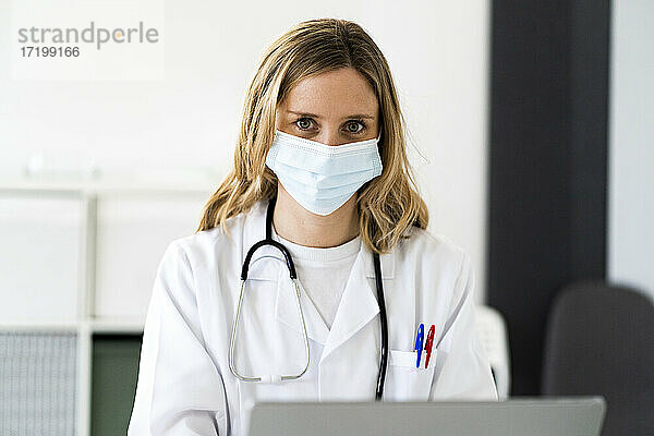 Blondes medizinisches Personal mit Laptop bei der Arbeit in einer medizinischen Klinik während COVID-19