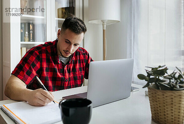 Junger männlicher Unternehmer beim Schreiben im Home Office