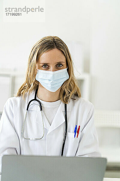 Weibliche medizinische Fachkraft mit Gesichtsschutz bei der Arbeit am Laptop in einer medizinischen Klinik