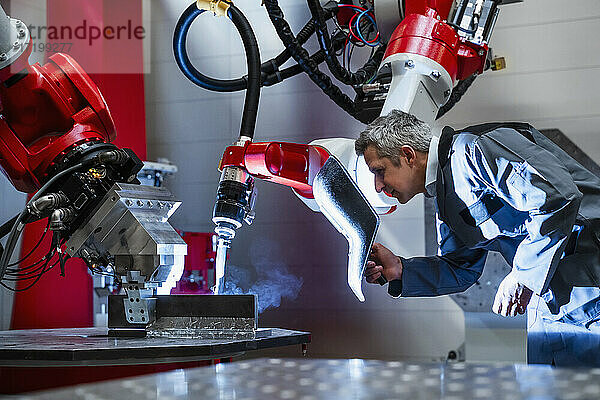 Älterer Arbeiter mit Schweißhelm bei der Arbeit an einem Roboter in einer Fabrik