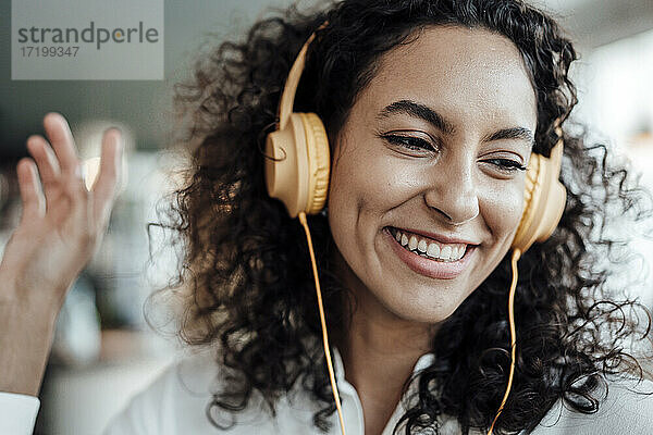 Glückliche Geschäftsfrau mit Kopfhörern  die lächelnd Musik in einem Café hört