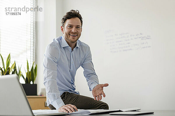 Lächelnder Geschäftsmann mit Dokument am Schreibtisch im Büro