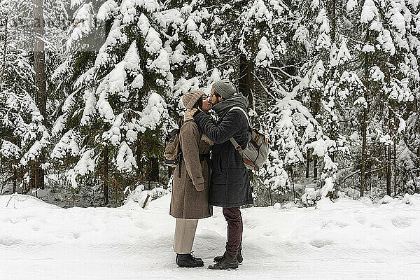 Junges Paar mit Rucksack  das sich küsst  während es im Wald steht