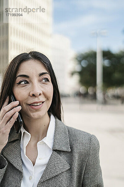 Nachdenkliche Geschäftsfrau  die in der Stadt mit einem Smartphone telefoniert