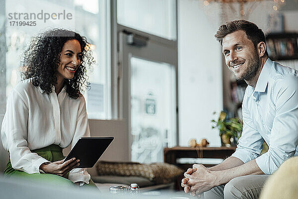 Geschäftsfrau mit digitalem Tablet  die einen Kollegen ansieht  während sie in einem Cafe sitzt