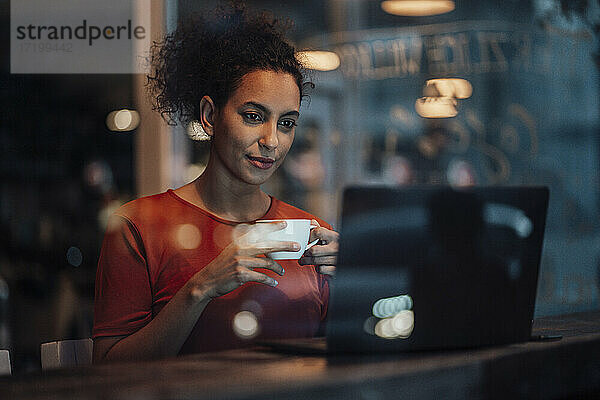 Junge Frau mit Kaffeetasse  die in einem Café sitzt und am Laptop arbeitet