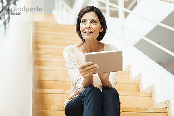 Ältere Geschäftsfrau mit digitalem Tablet  die auf einer Treppe im Korridor sitzt