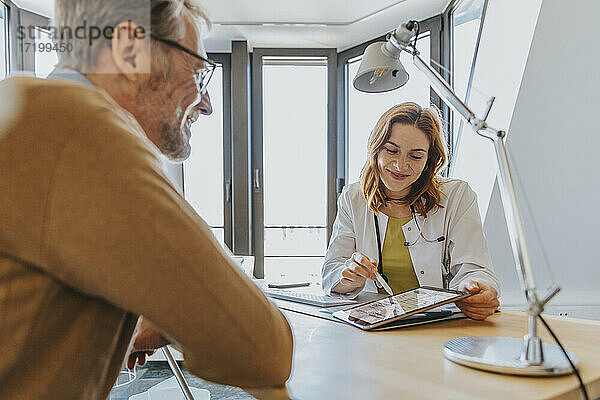 Allgemeinmediziner erklärt Patienten über ein digitales Tablet  während er in der Klinik sitzt