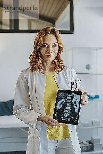 Mid adult doctor showing x-ray image on digital tablet while standing at clinic