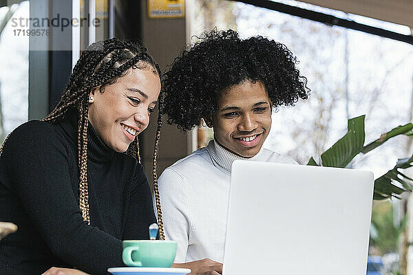 Lächelnde Studenten  die einen Laptop in einem Straßencafé benutzen