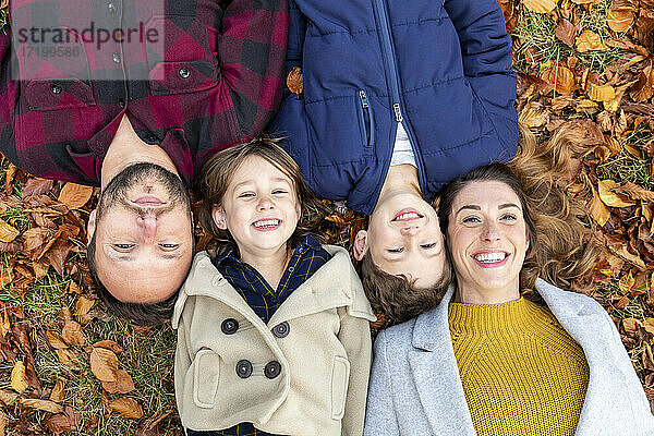 Familie lächelt  während sie sich auf einem gefallenen Blatt im Wald im Herbst ausruht