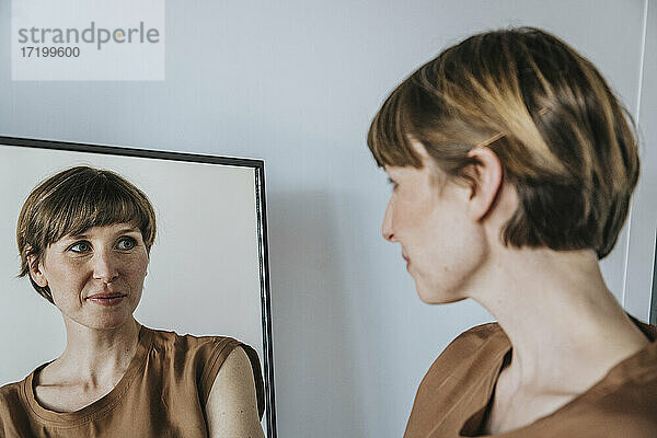 Nachdenkliche Frau betrachtet ihre Reflexion im Spiegel