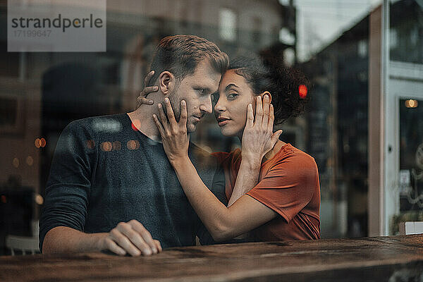 Romantisches Paar  das sich im Café berührt  gesehen durch ein Fenster