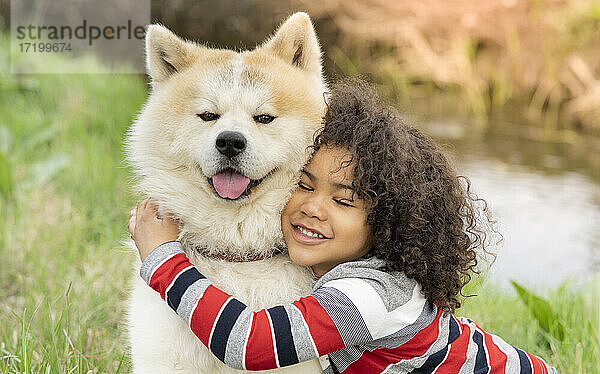 Lächelnder Junge umarmt Hund in der Natur