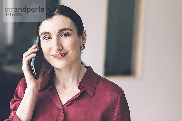 Lächelnde Unternehmerin  die zu Hause mit einem Mobiltelefon spricht