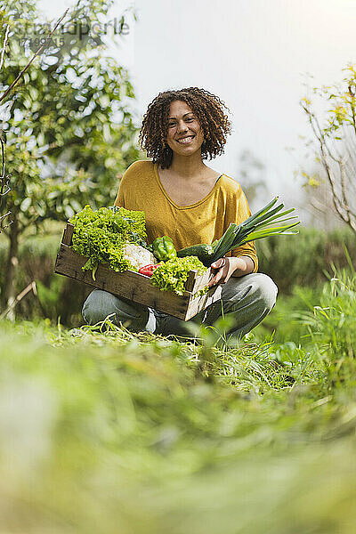 Lächelnde Frau hockt und hält Blattgemüse gegen den Himmel im Garten