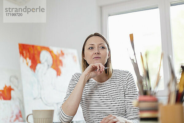 Nachdenkliche Frau mit Stift im Heimstudio sitzend