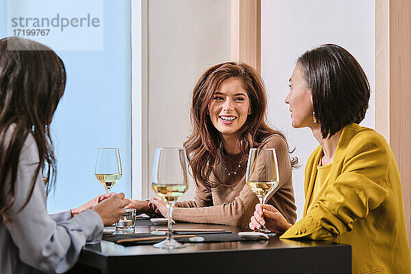 Junge Freundinnen mit Weingläsern am Tisch in einem Restaurant