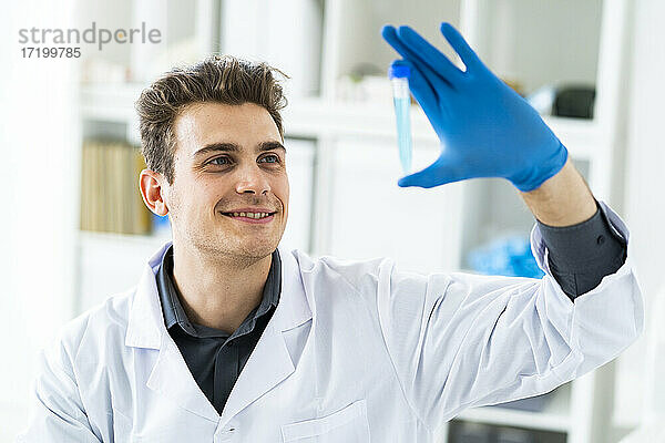 Lächelnder männlicher Wissenschaftler  der eine Flüssigkeit im Reagenzglas untersucht