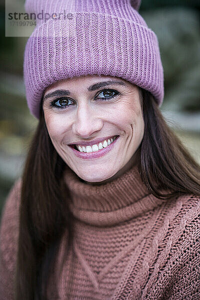 Porträt einer schönen Frau mit rosa Strickmütze  die in die Kamera lächelt
