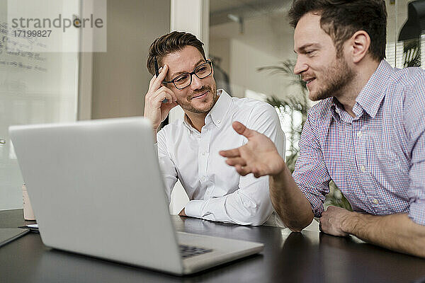 Geschäftsmann mit männlichem Kollegen diskutiert über Laptop im Büro