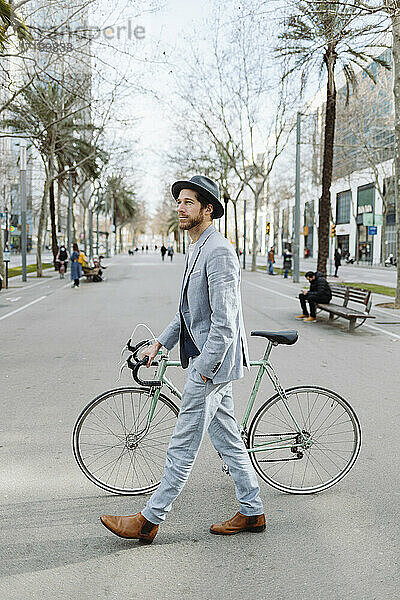 Männlicher Berufstätiger mit Hut beim Spaziergang mit dem Fahrrad in der Stadt