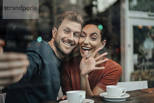 Lächelndes Paar  das einen Videoanruf auf dem Mobiltelefon betrachtet  während es im Café sitzt