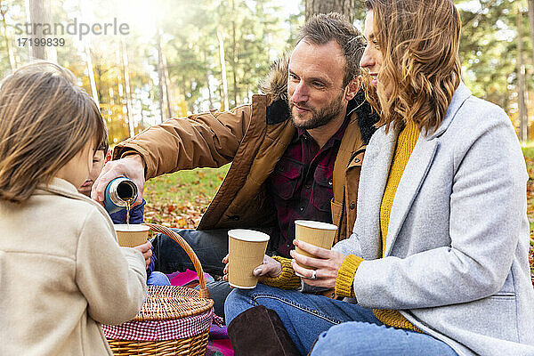 Vater gießt Kaffee in die Tasse seiner Tochter  während er mit seiner Familie im Wald sitzt
