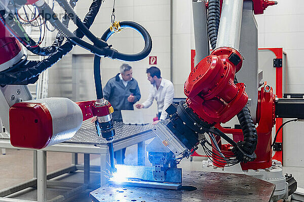 Roboterarm schweißt  während männliche Ingenieure in der Fabrik diskutieren
