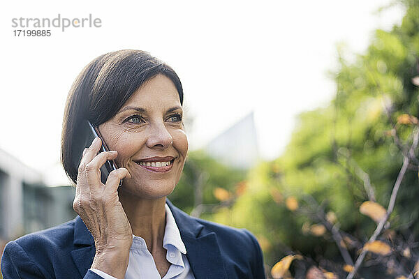 Lächelnde Unternehmerin  die im Büropark mit einem Mobiltelefon spricht