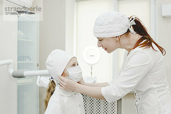 Eine Zahnärztin setzt einem kleinen Mädchen eine Gesichtsmaske auf