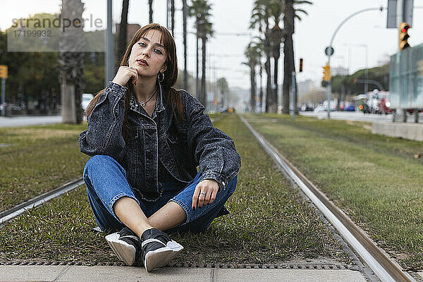 Selbstbewusste junge Frau  die an der Straßenbahnhaltestelle auf dem Gleis sitzt