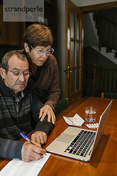 Älterer Mann mit Sozialarbeiter  der zu Hause am Laptop in einem Buch schreibt
