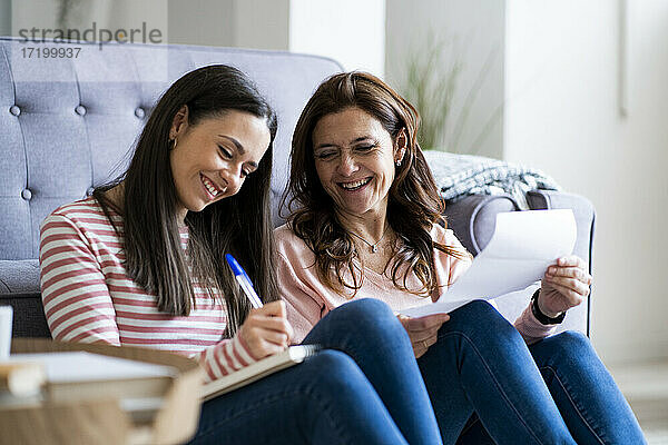 Lächelnde Mutter und Tochter prüfen Rechnungen  während sie auf dem Sofa im Wohnzimmer sitzen