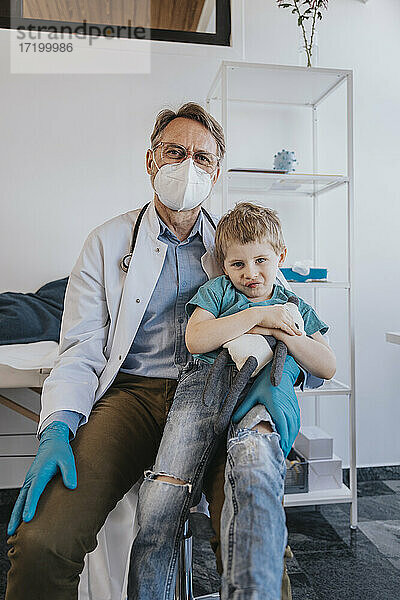 Kinderarzt sitzt mit einem Jungen auf dem Schoß im Untersuchungsraum