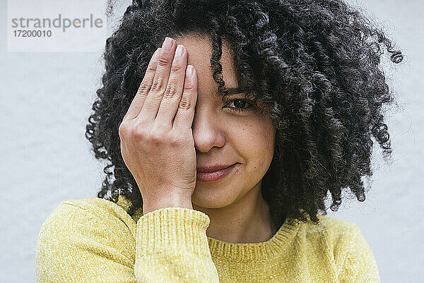 Lockig behaarte Frau  die ihre Augen vor einer weißen Wand verdeckt