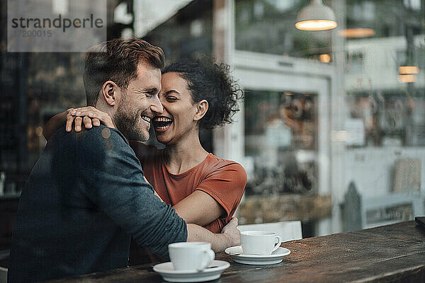 Fröhliche Frau sitzt mit dem Arm um einen Mann im Cafe