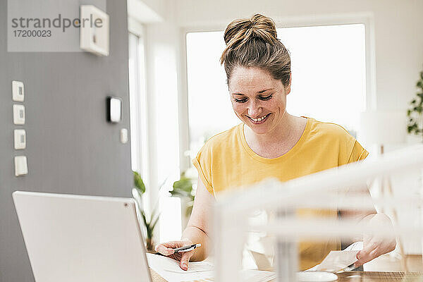 Lächelnde Geschäftsfrau  die an einem Dokument arbeitet  während sie am Schreibtisch sitzt