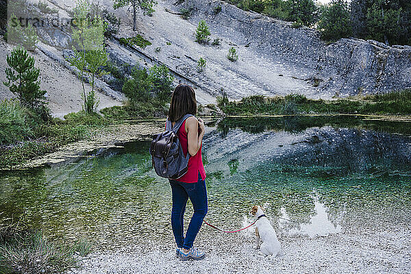 Frau mit Rücken neben Hund am See stehend