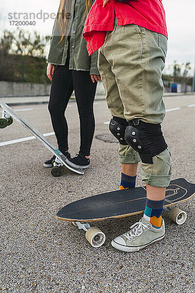 Frau mit Skateboard  die einen Knieschutz trägt  während sie neben einer Freundin auf der Straße steht