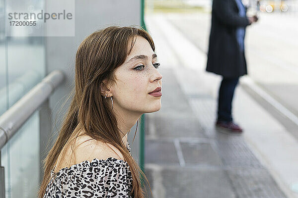 Junge Frau mit braunen Haaren sitzt an einer Straßenbahnhaltestelle