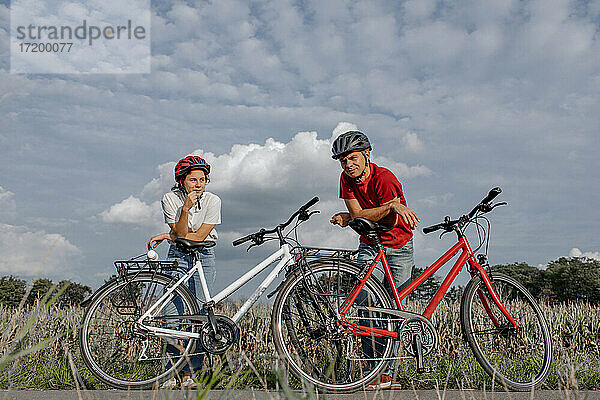 Tochter mit Vater  der sich auf ein Fahrrad stützt  während er auf einem landwirtschaftlichen Feld vor bewölktem Himmel steht