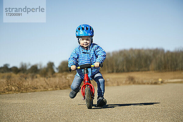 Niedlicher Junge mit Fahrradhelm auf dem Fahrrad an einem sonnigen Tag auf der Straße