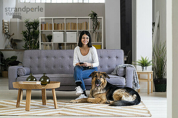 Lächelnde junge Frau mit Haushund im Wohnzimmer