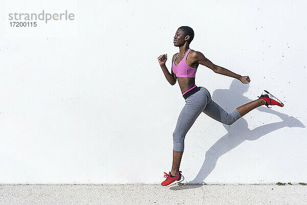 Junge Sportlerin läuft gegen eine weiße Wand an einem sonnigen Tag