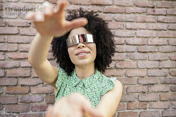 Junge Afro-Frau mit futuristischer Sonnenbrille vor einer Backsteinmauer