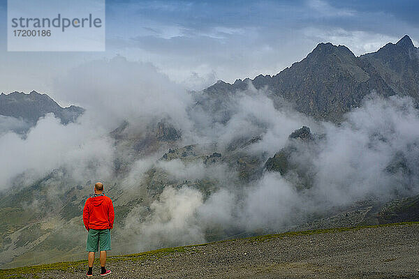 Mann in leuchtend roter Jacke betrachtet den Nebel  der über dem Col du Tourmalet-Pass schwebt  Frankreich