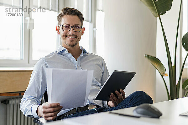Selbstbewusster Geschäftsmann mit Dokument und digitalem Tablet im Büro