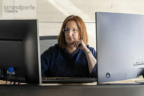 Reife Geschäftsfrau mit Brille arbeitet am Computer und sitzt am Schreibtisch im Büro