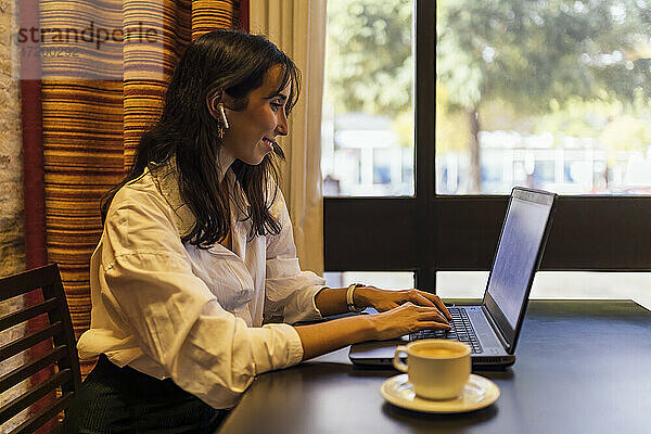 Lächelnde Unternehmerin  die einen Laptop benutzt  während sie in einem Café sitzt